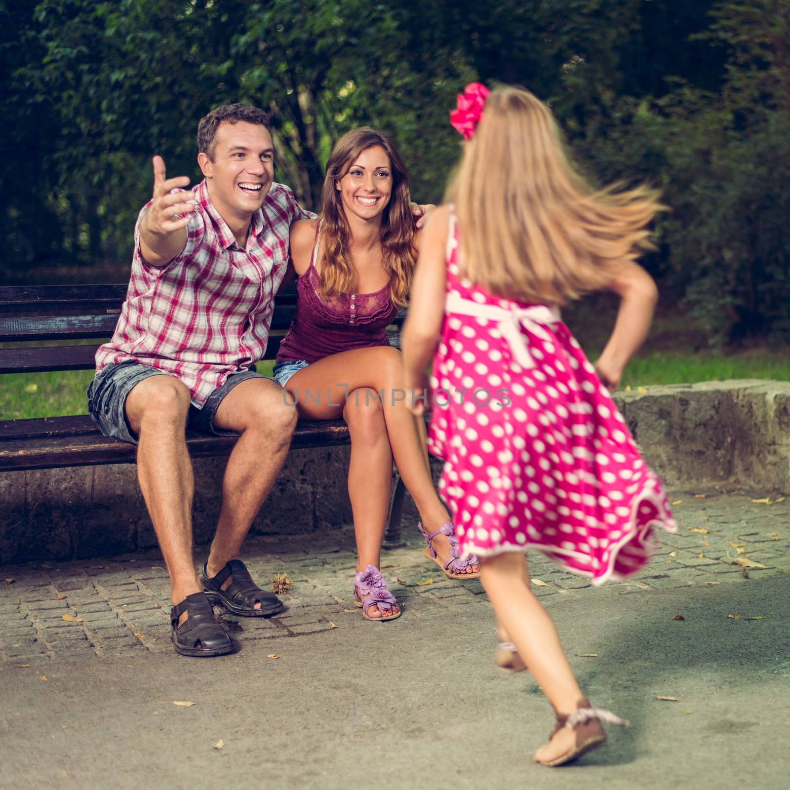 Beautiful little girl race to embrace her parents in the park.