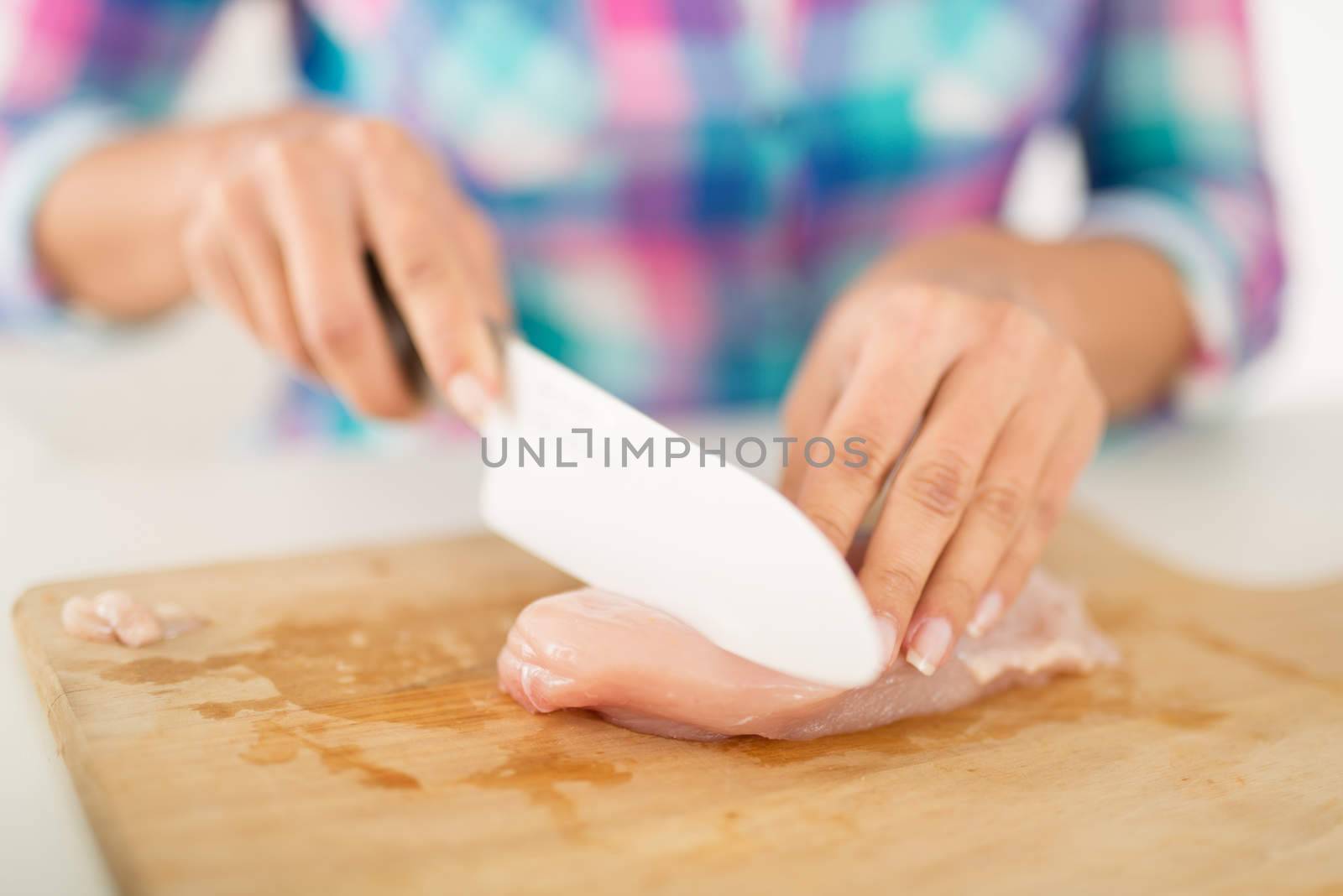 Close-up of a female Hands cutting chicken filet on the kitchen board.