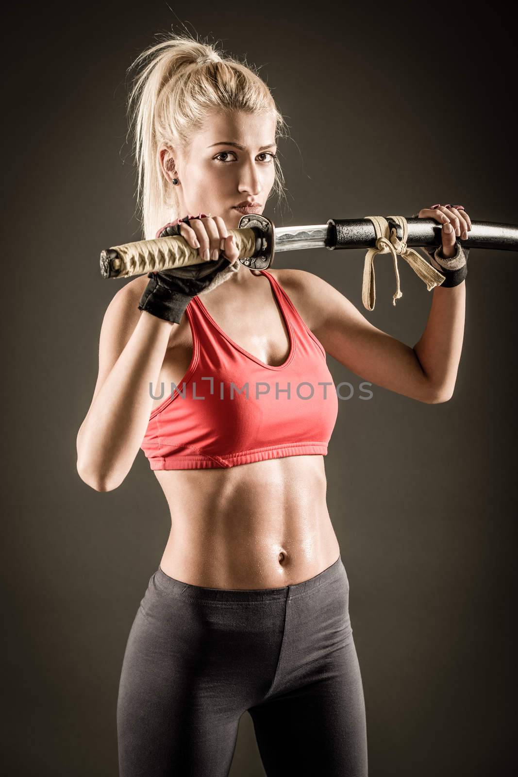 Pretty girl with a serious expression on her face drawing katana and looking at the camera. 