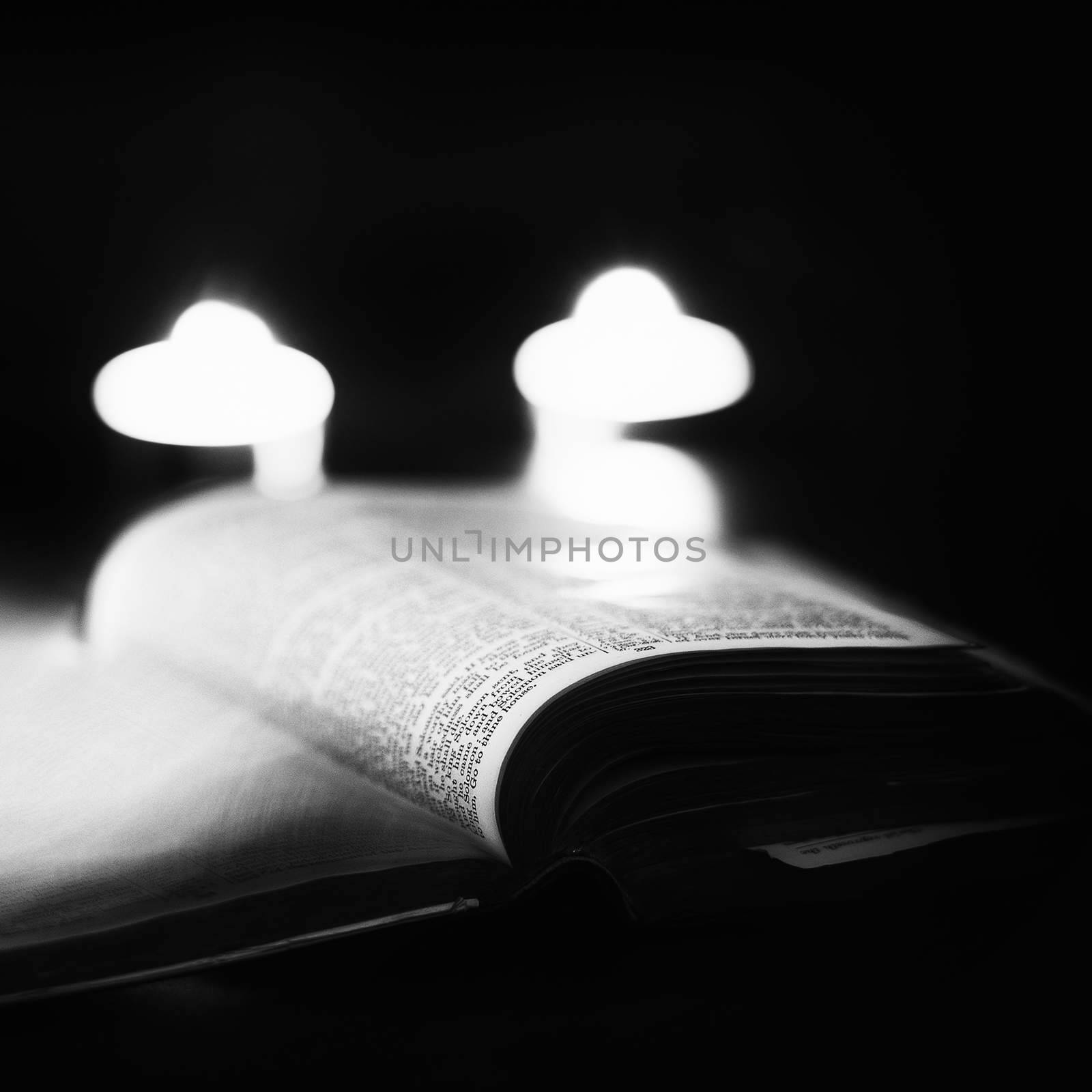 Bible with candles in the background. Low light high contrast black and white image.