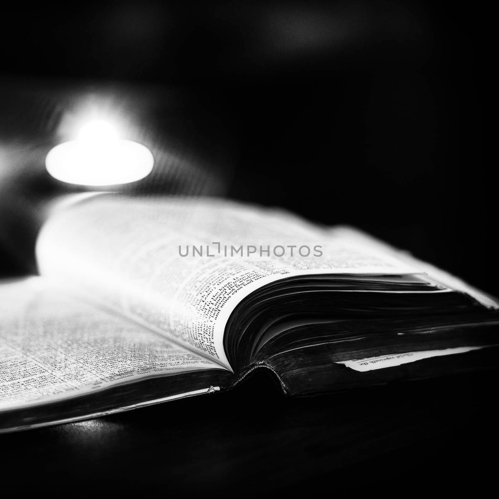 Bible with candles in the background. Low light high contrast black and white image.