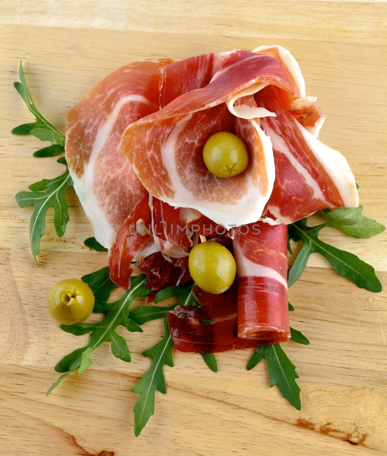 Jamon Appetizer with Green Olives and Arugula Leafs closeup on Wooden Cutting Board
