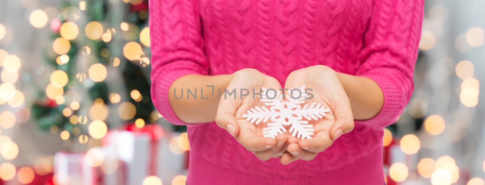 christmas, holidays and people concept - close up of woman in pink sweater holding snowflake over tree lights background