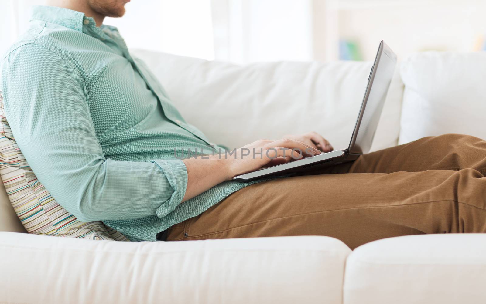 technology, home and lifestyle concept - close up of man working with laptop computer and sitting on sofa at home