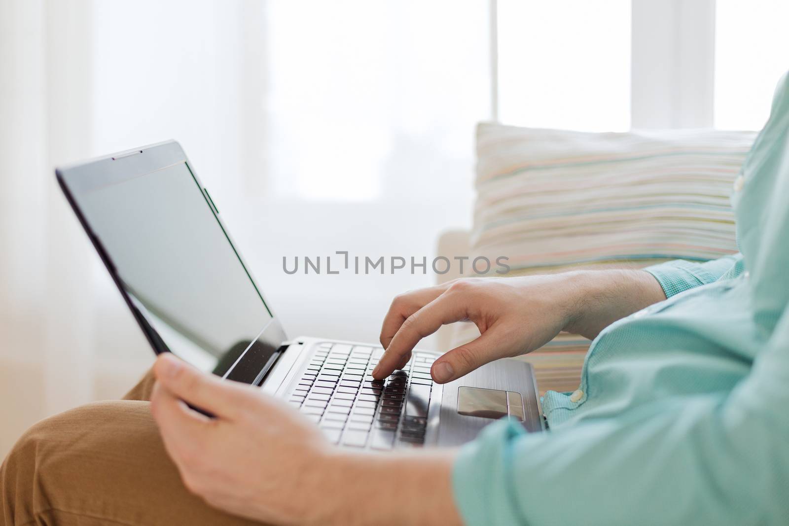 technology, home and lifestyle concept - close up of man working with laptop computer and sitting on sofa at home