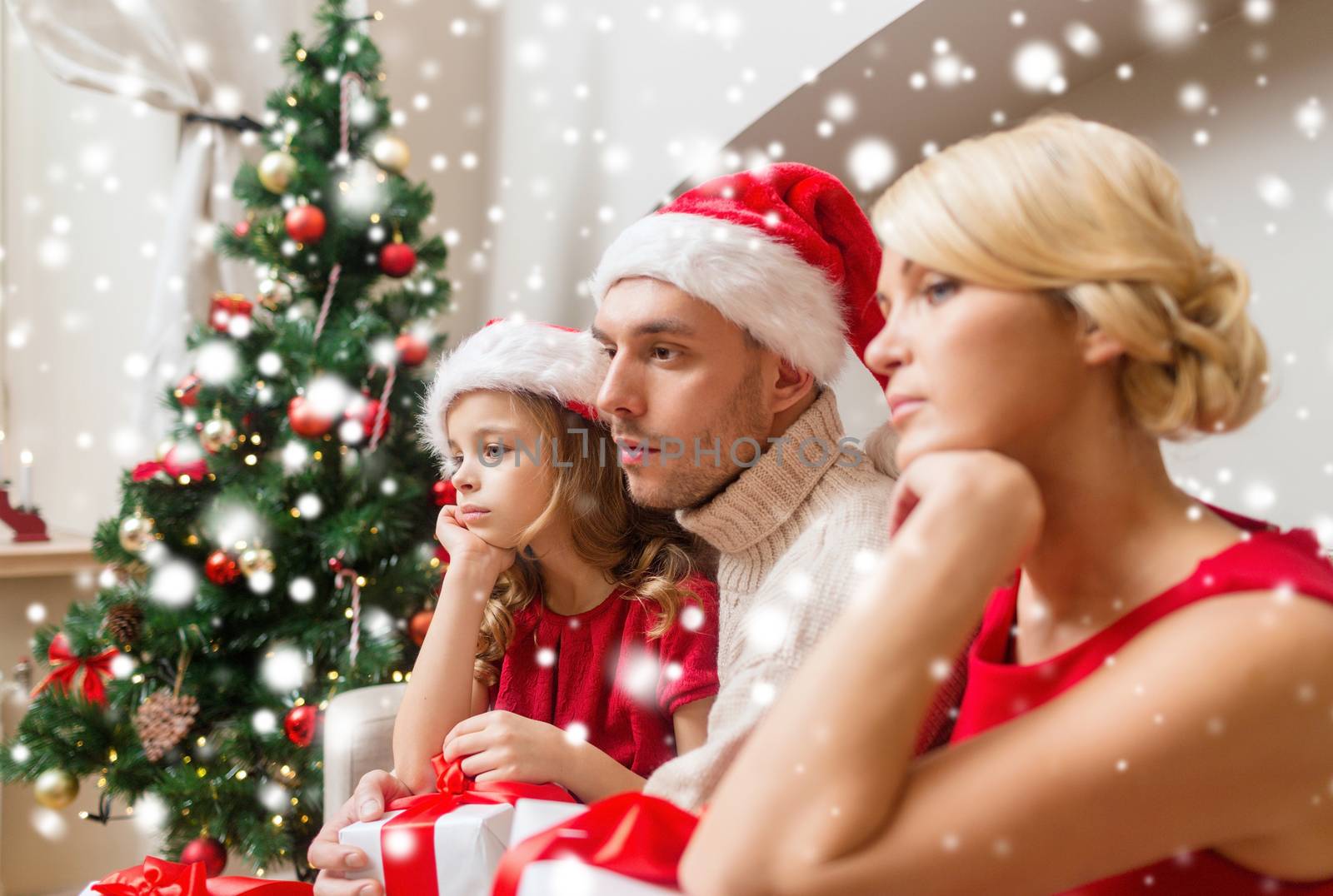 christmas, holidays, sadness and people concept - sad family in santa helper hats with gift boxes at home