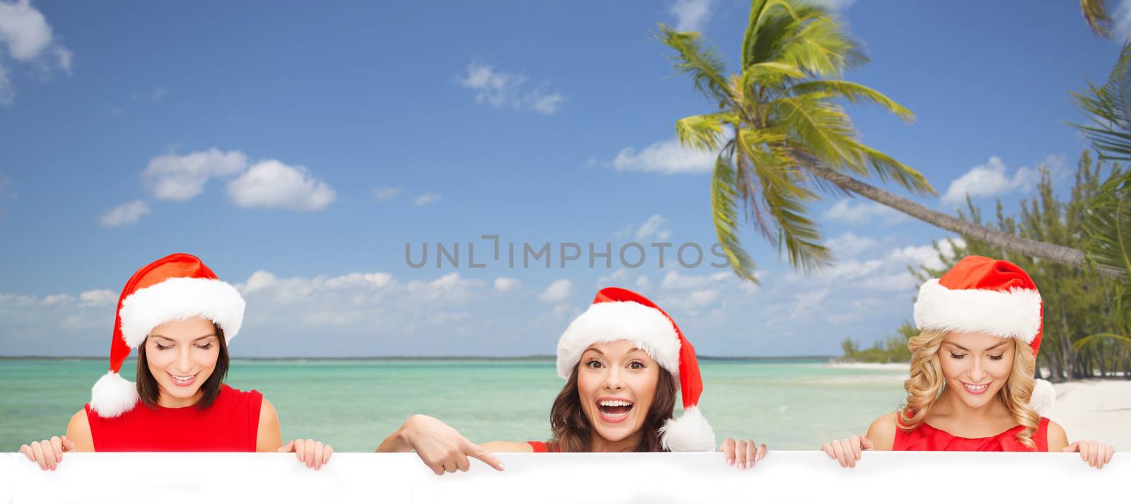 christmas, x-mas, people, advertisement and sale concept - happy women in santa helper hat with blank white board over tropical beach background