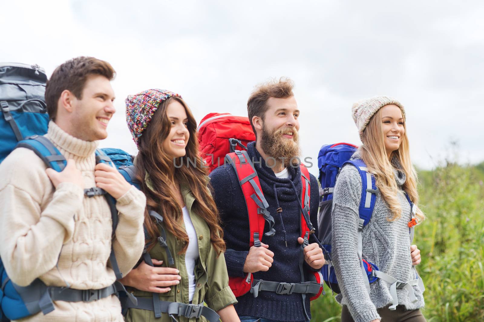 adventure, travel, tourism, hike and people concept - group of smiling friends walking with backpacks