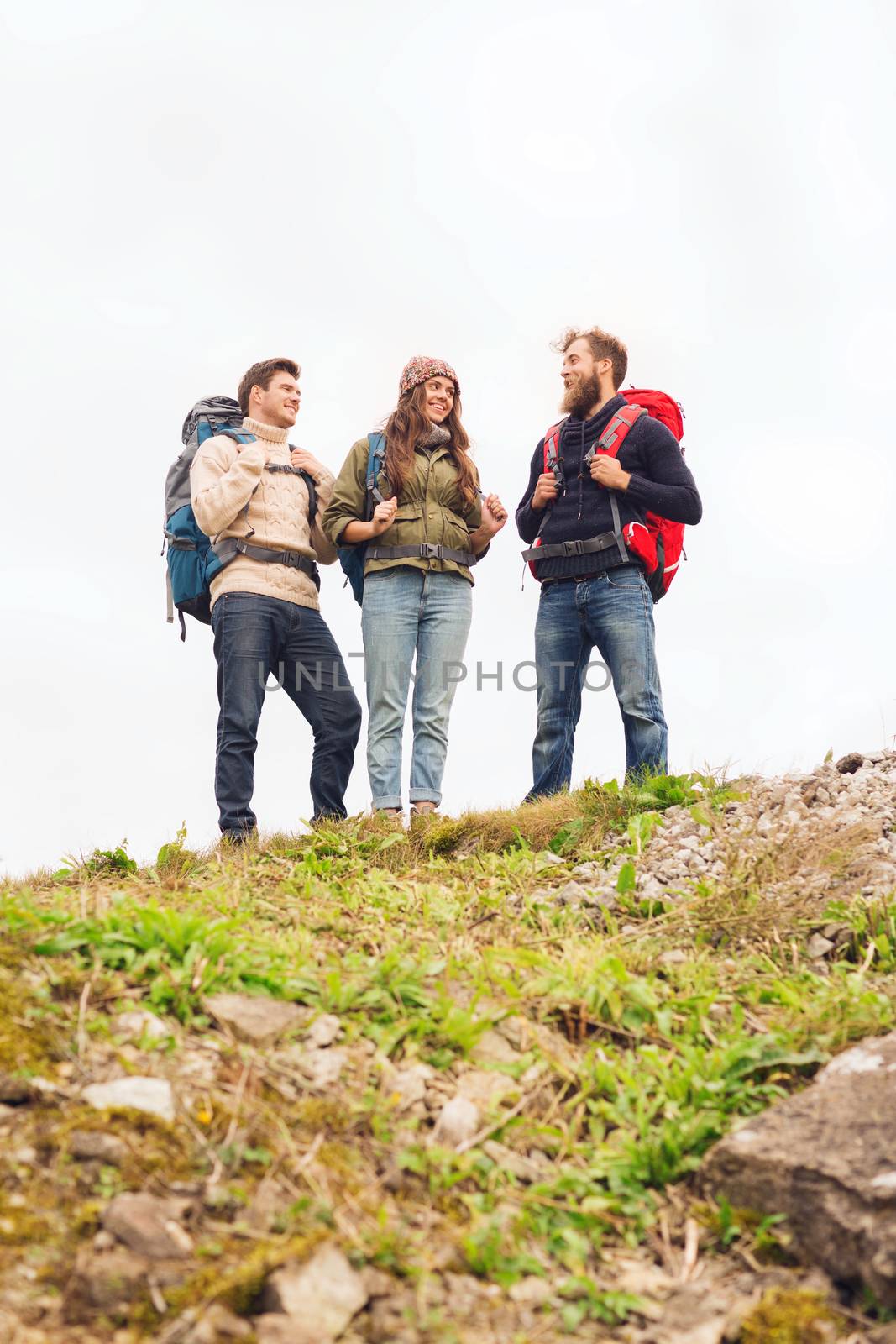 adventure, travel, tourism, hike and people concept - group of smiling friends with backpacks standing on hill and talking outdoors