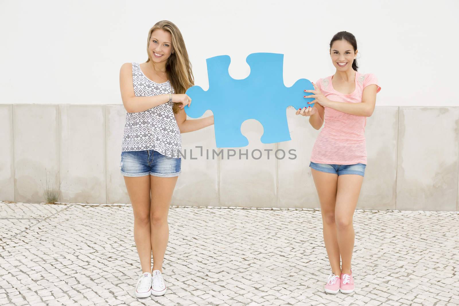 Two beautiful teenage students holding a giant puzzle piece 