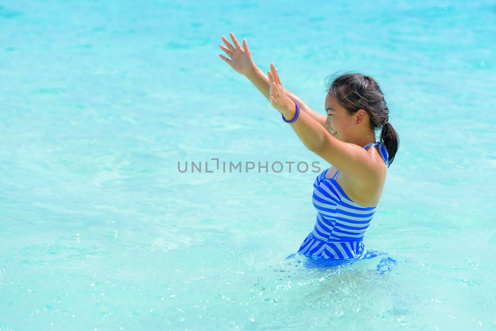 Girl in a blue swimsuit playing splashing water at the sea near beach with happiness during summer at Koh Miang Island, Mu Ko Similan National Park, Phang Nga province, Thailand