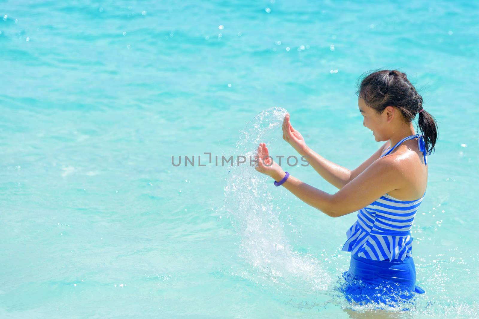 Girl in a blue swimsuit playing splashing water at the sea near beach with happiness during summer at Koh Miang Island, Mu Ko Similan National Park, Phang Nga province, Thailand