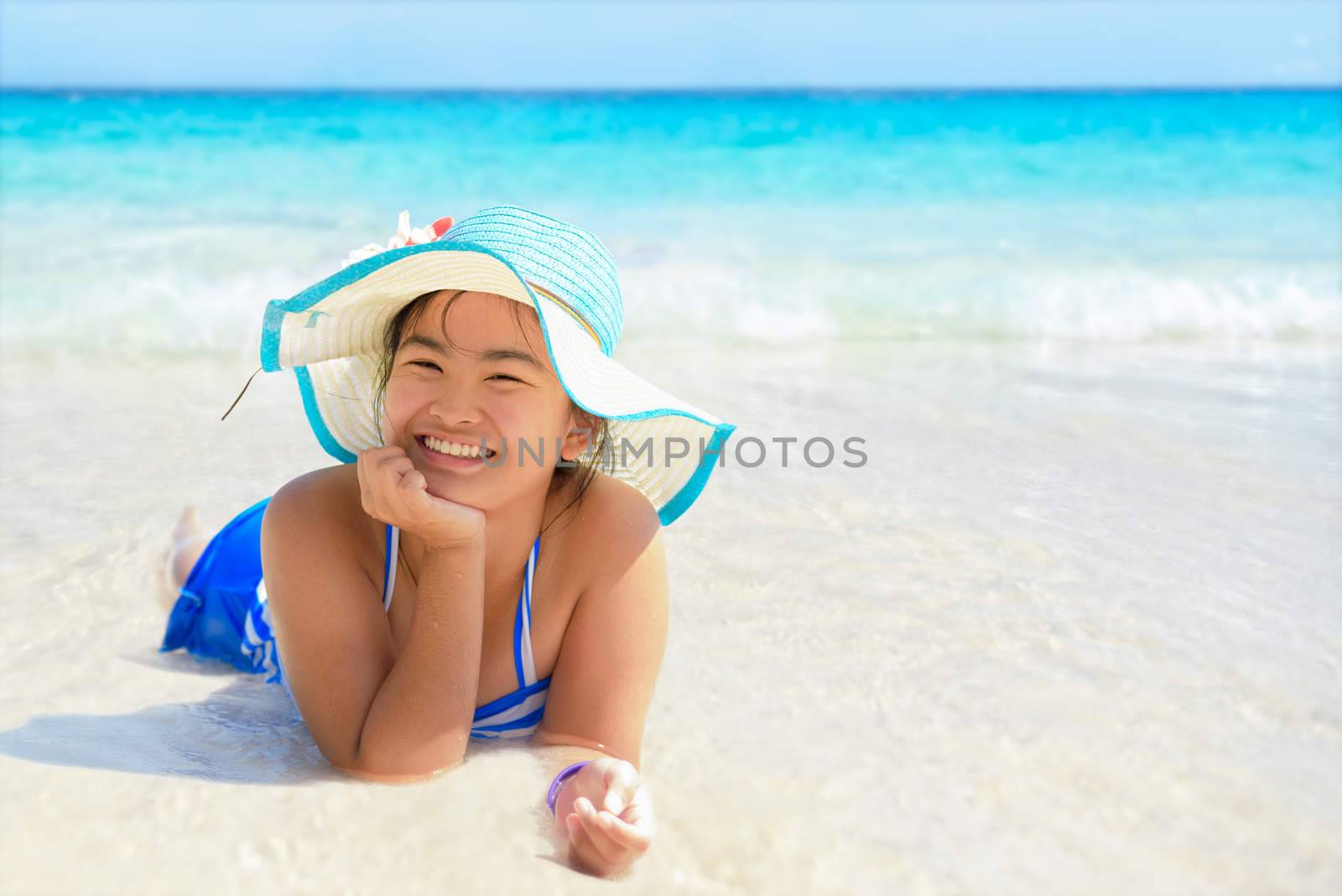 Girl in swimsuit wearing a blue hat lying in the sea with a happy face on the beach during summer at Koh Miang Island, Mu Ko Similan National Park, Phang Nga province, Thailand