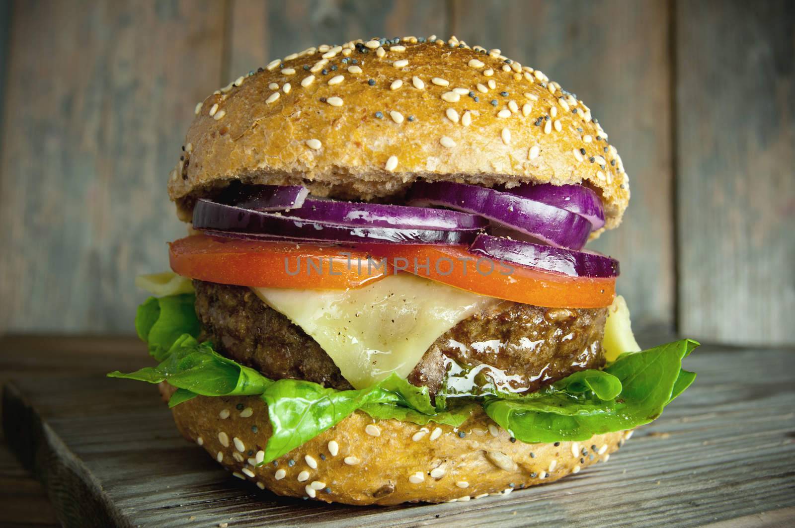 Gourmet burger with cheese, tomato and onion filling on top of a wooden chopping board