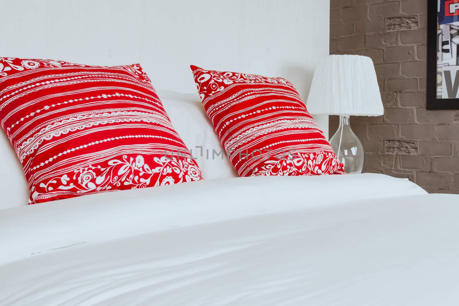 Red pillow on bedroom with white bed sheet and lamp by FrameAngel