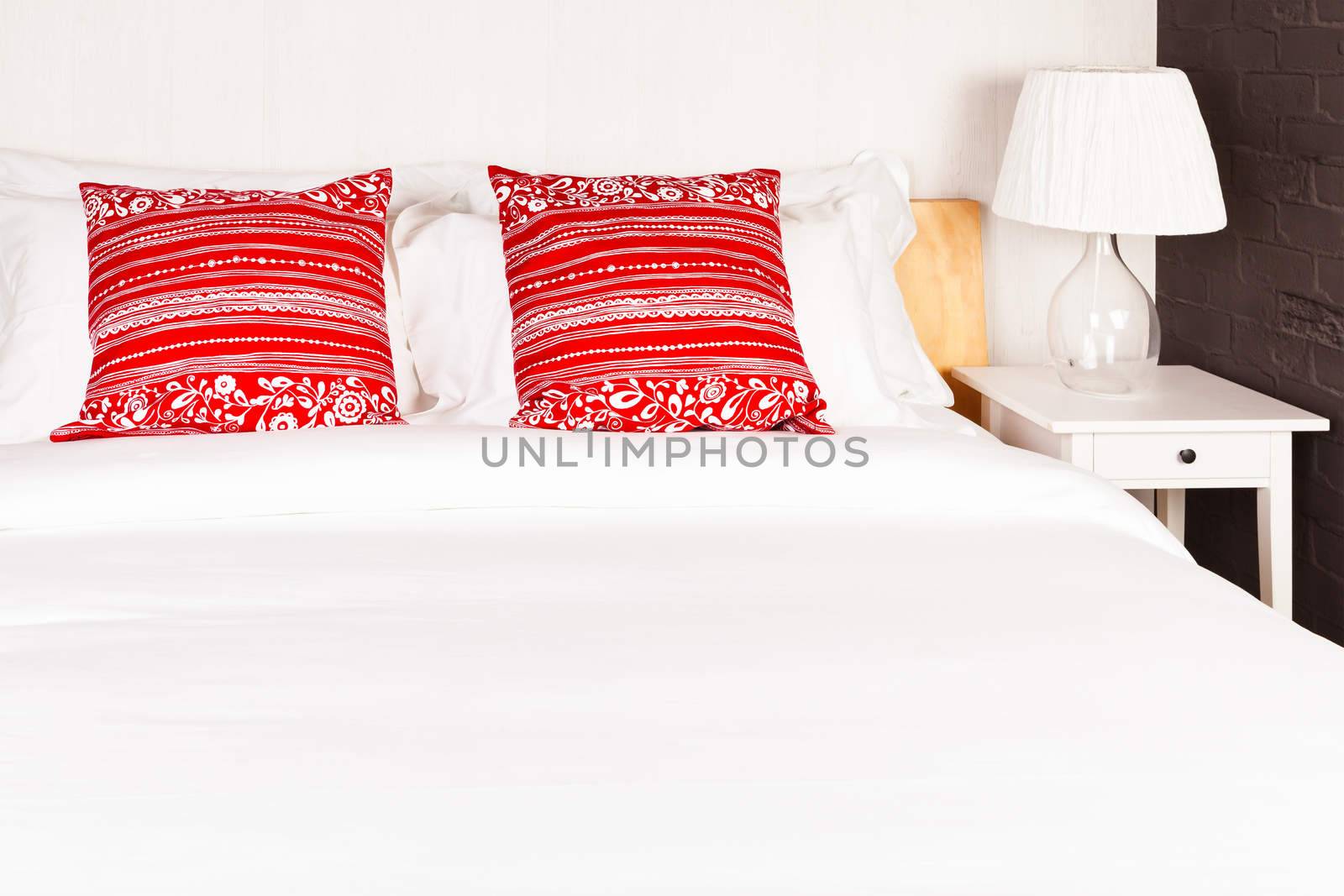 Red pillow on bedroom with white bed sheet and lamp