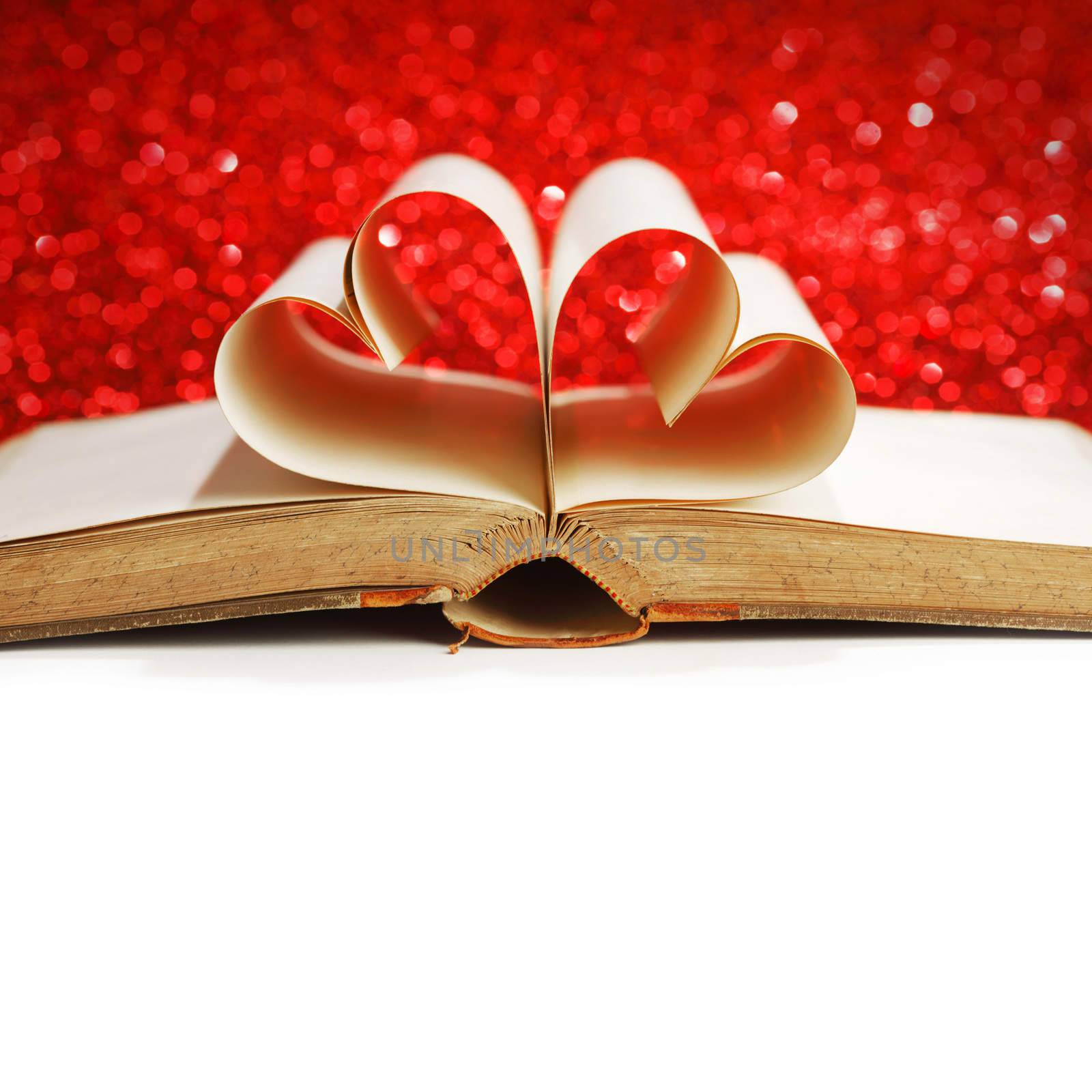 Pages of open book rolled in heart shape on glitter background