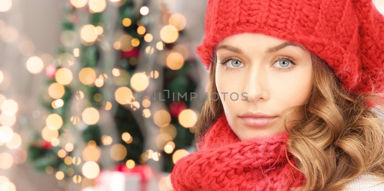 happiness, winter holidays and people concept - close up of young woman in red hat and scarf over christmas tree lights background