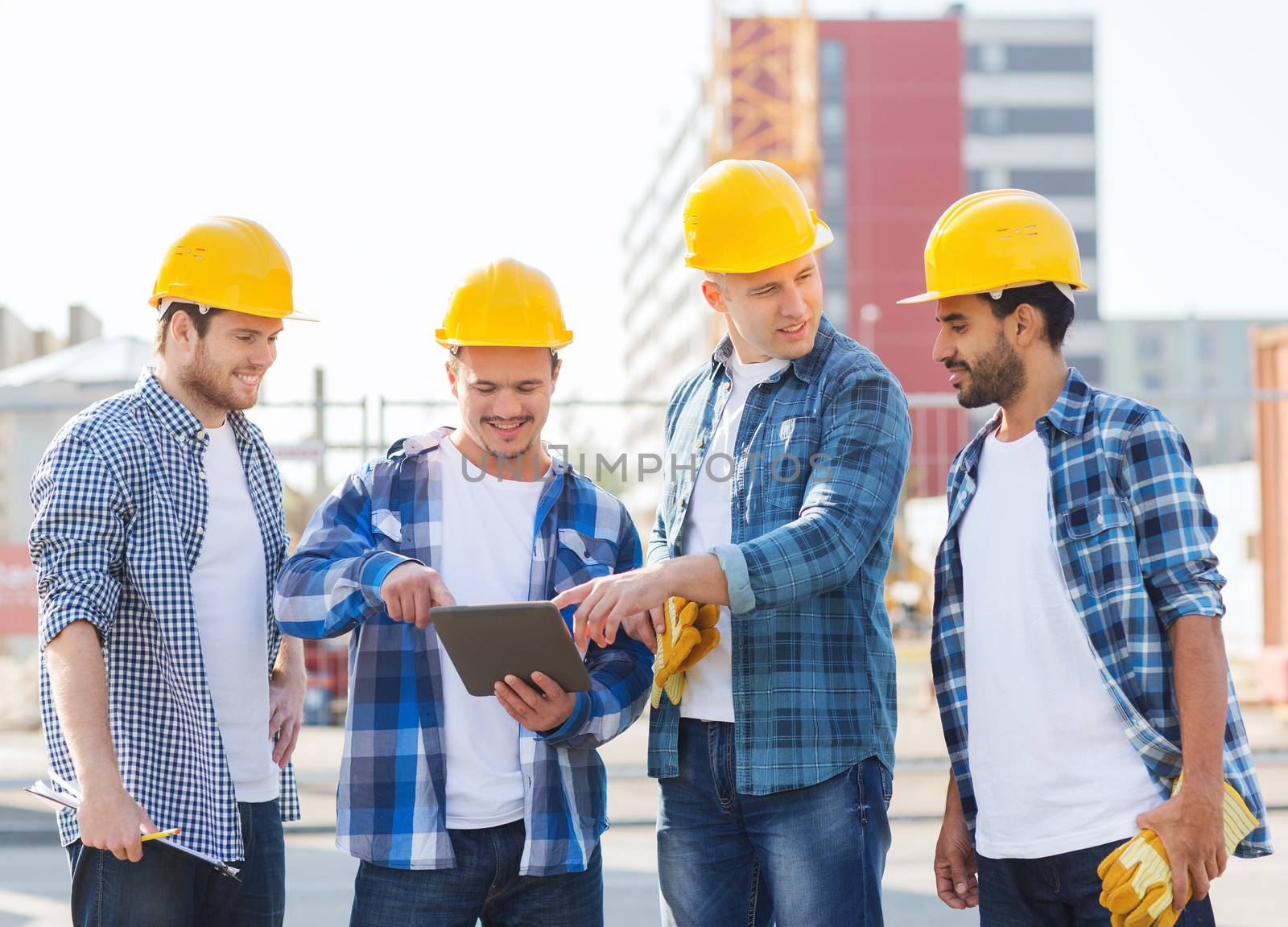 business, building, teamwork, technology and people concept - group of smiling builders in hardhats with tablet pc computer and clipboard outdoors