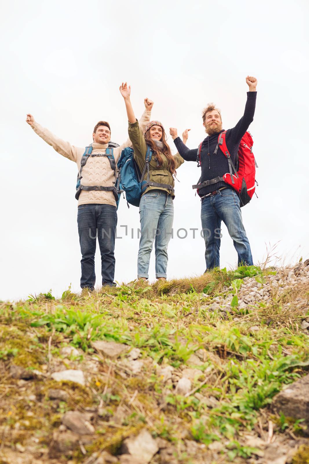 travel, tourism, hike, gesture and people concept - group of smiling friends with backpacks raising hands outdoors