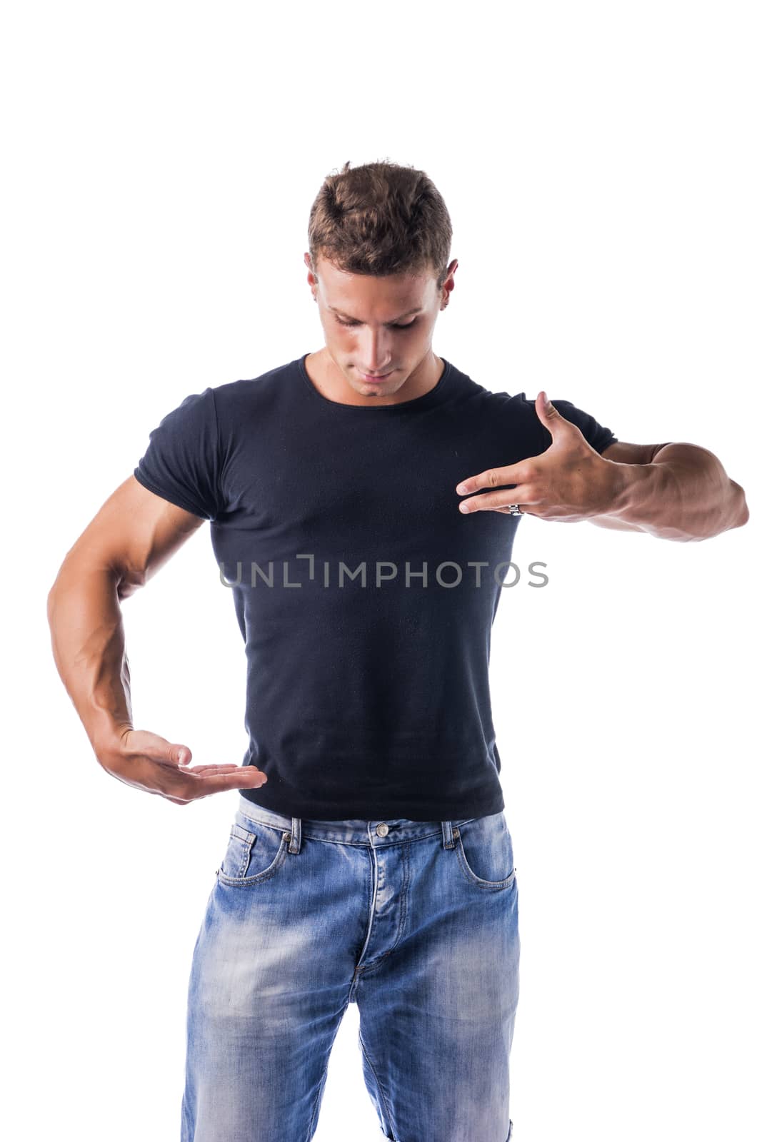 Handsome Muscular Young Man Wearing Casual Black Shirt and Jeans Showing Empty Copy Space on His T-Shirt with Hands Pose While Looking at It at the Studio. Isolated on White Background.