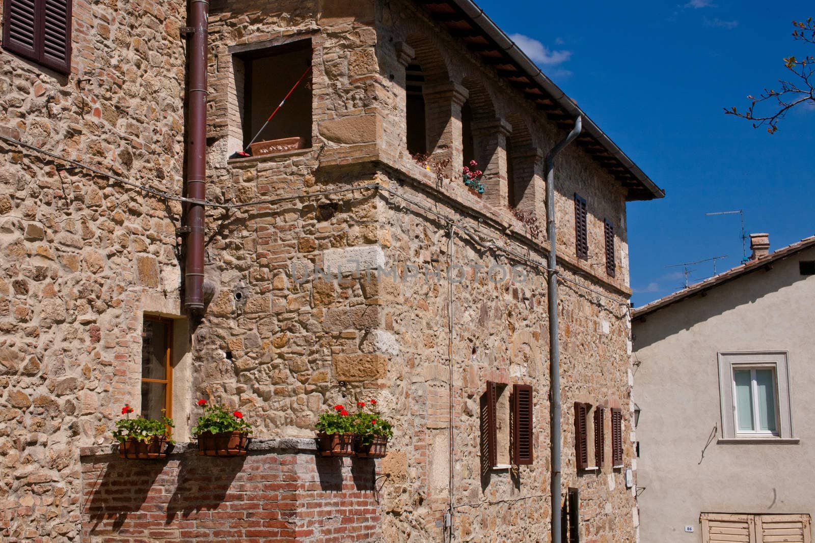 An old stone building and red flowers in San Quirico d'Orcia in Italy
