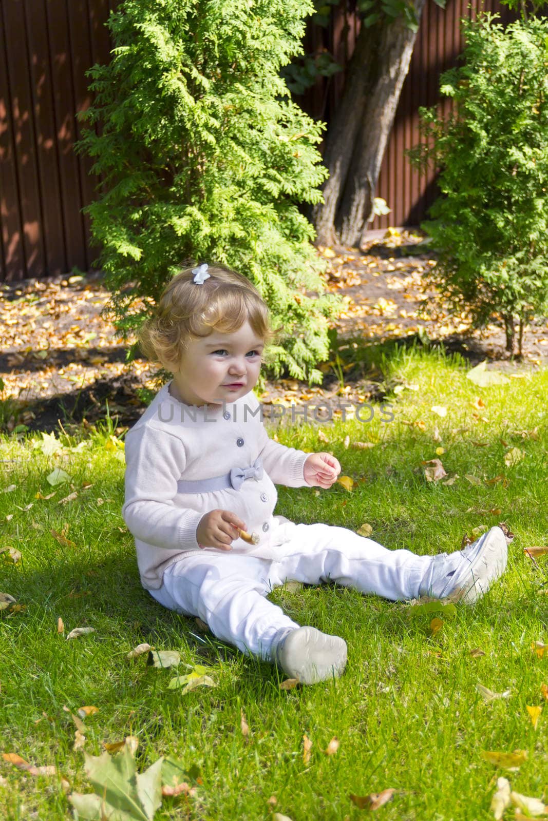 Baby girl with curly hair sitting on green grass