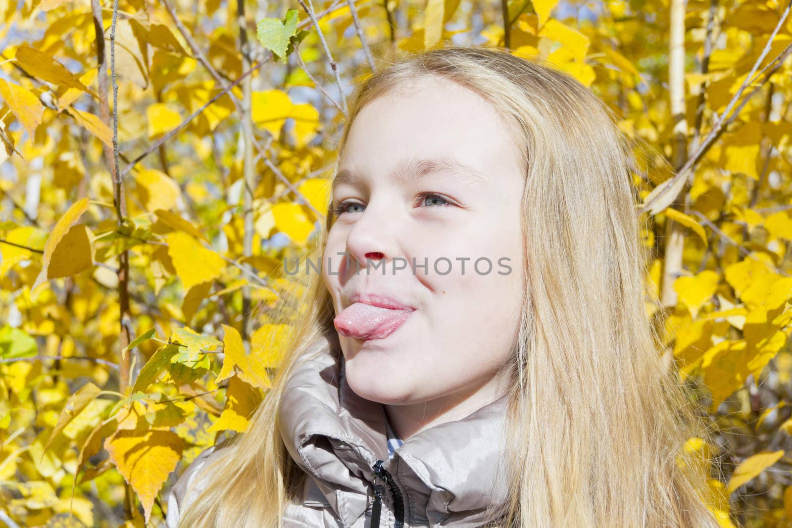 Autumn portrait of blond girl in sunlight put out tongue
