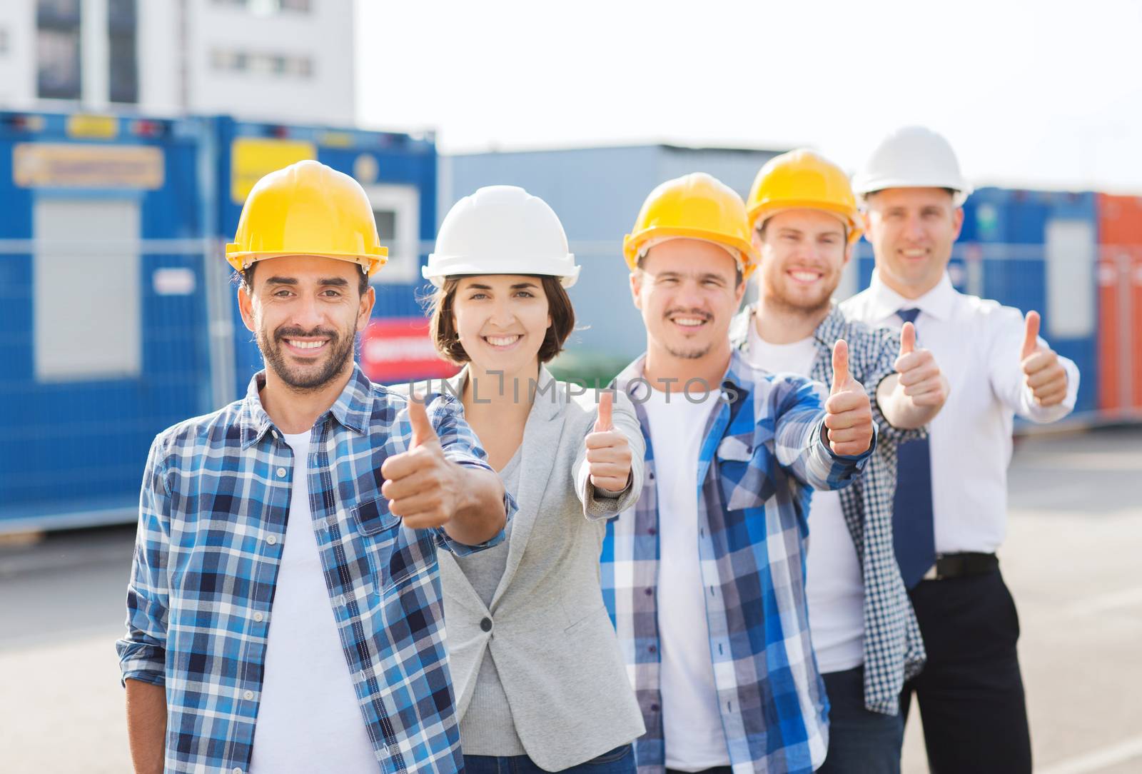 business, building, teamwork, gesture and people concept - group of smiling builders in hardhats showing thumbs up outdoors