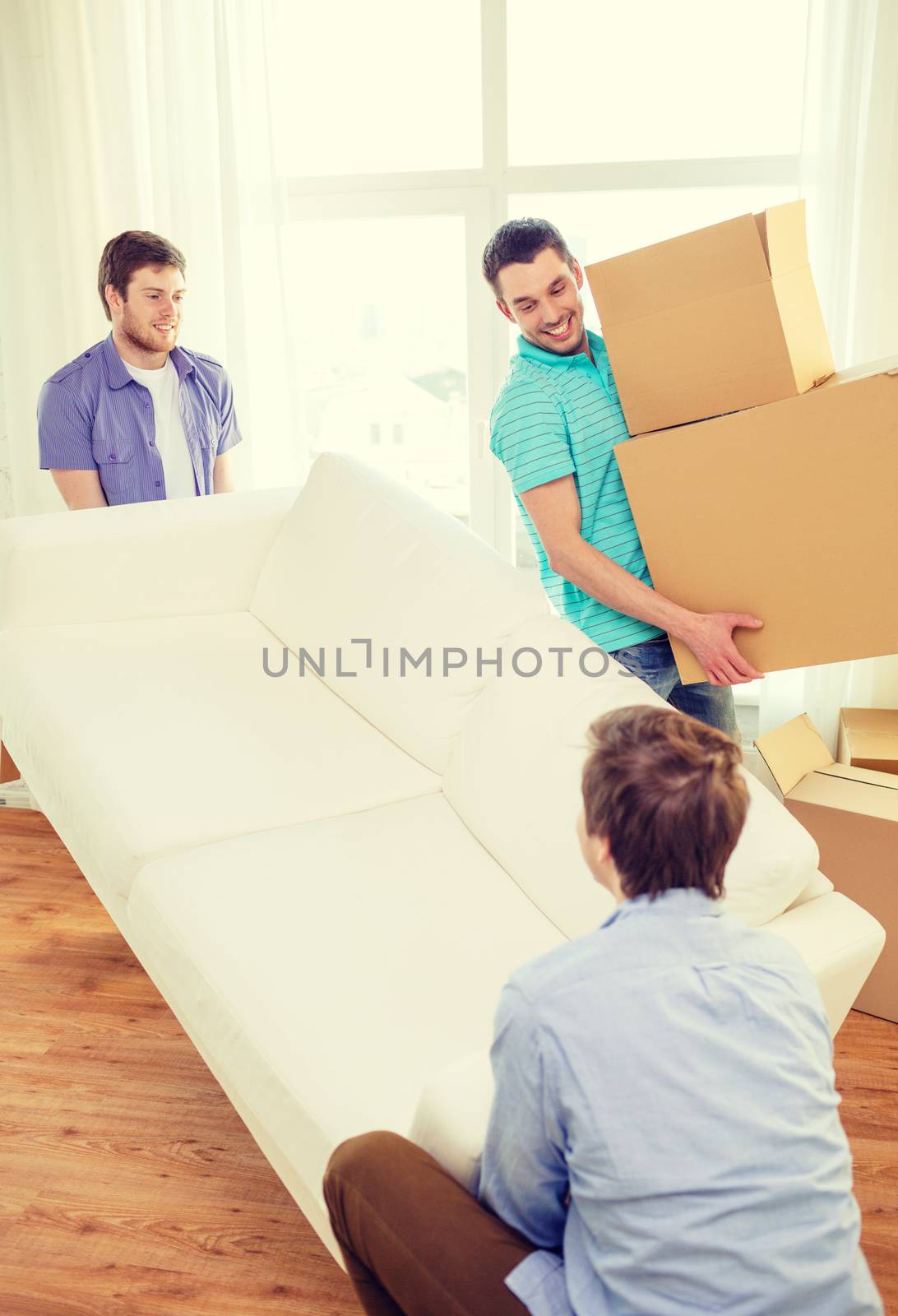 moving, real estate and friendship concept - smiling male friends with sofa and boxes at new home