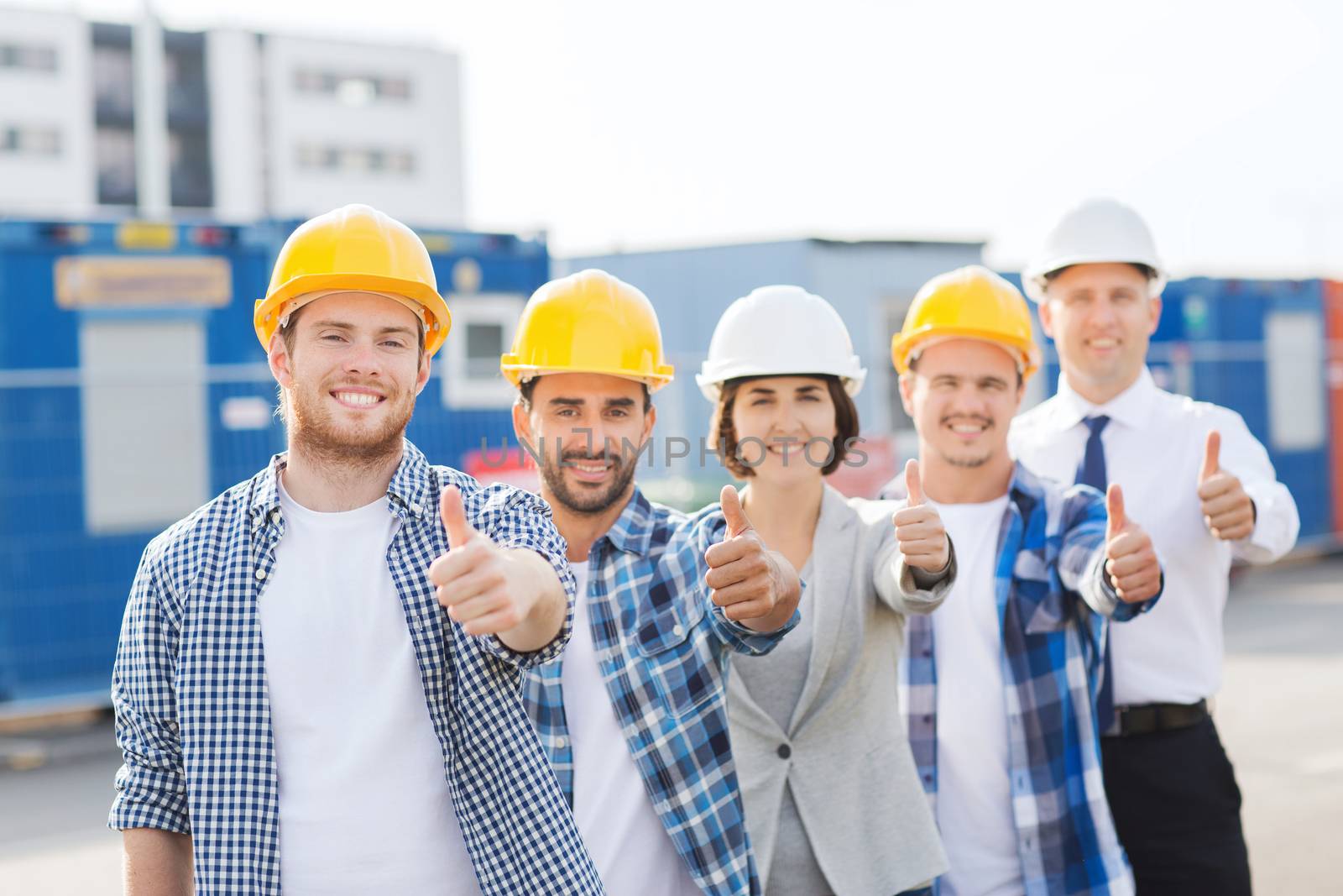 group of smiling builders in hardhats outdoors by dolgachov