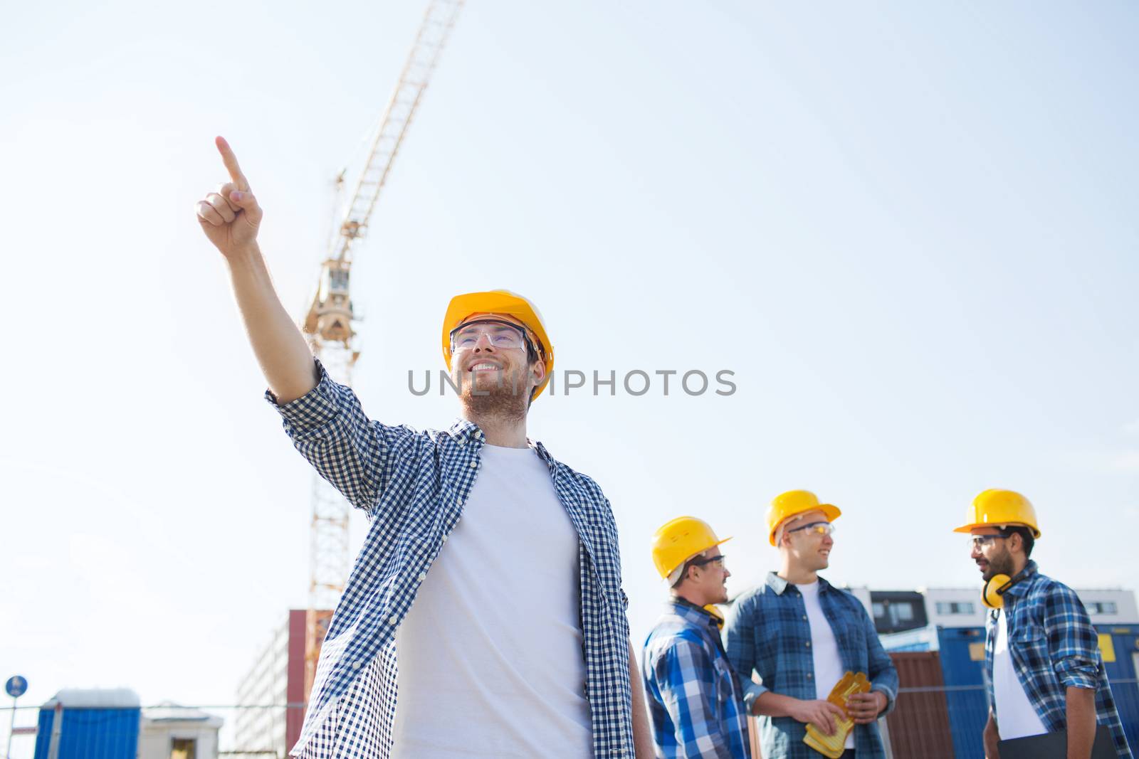 business, building, teamwork and people concept - group of smiling builders in hardhats pointing finger outdoors