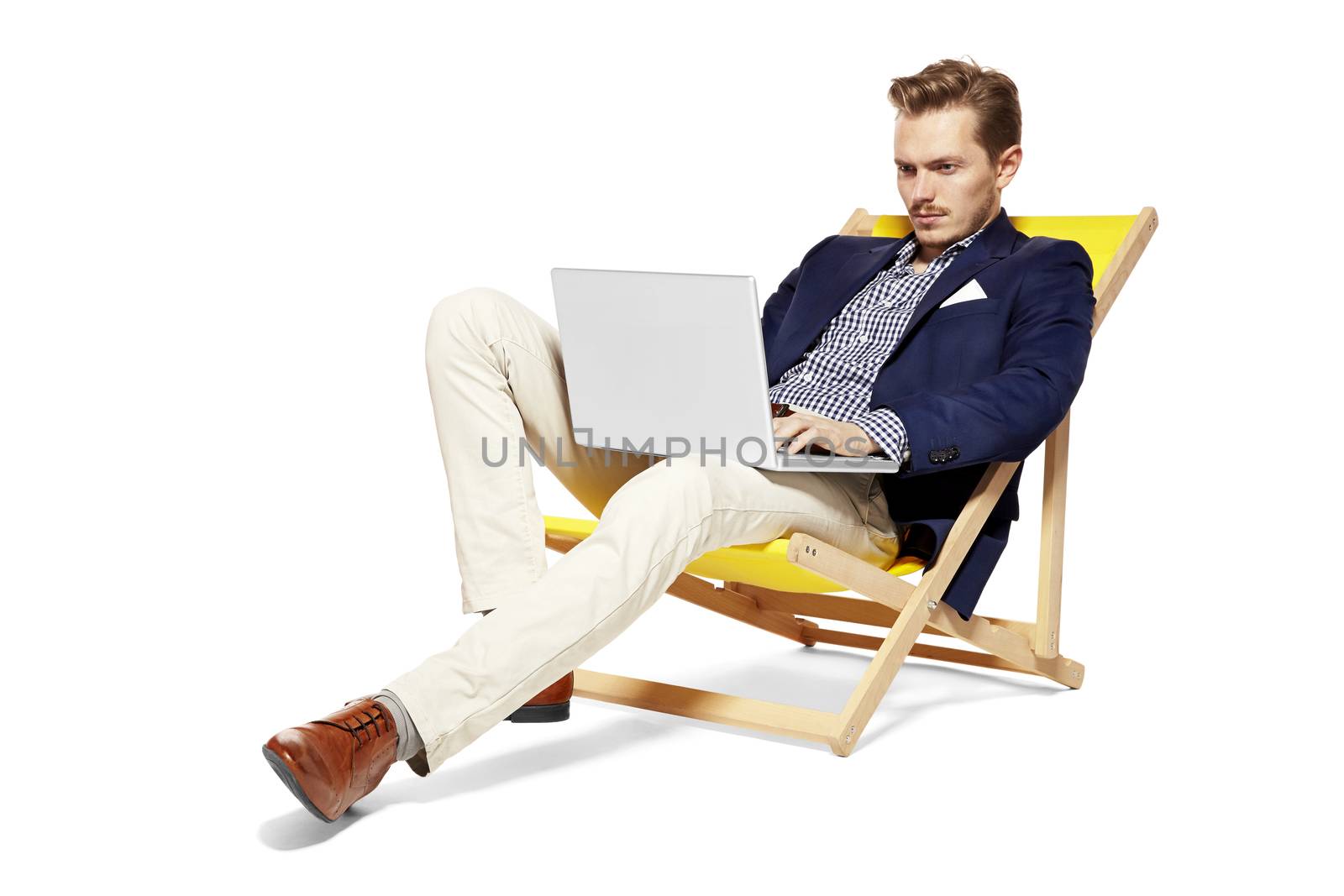 Handsome man sitting on a sunbed and working on a computer. Isolated on white background. 

