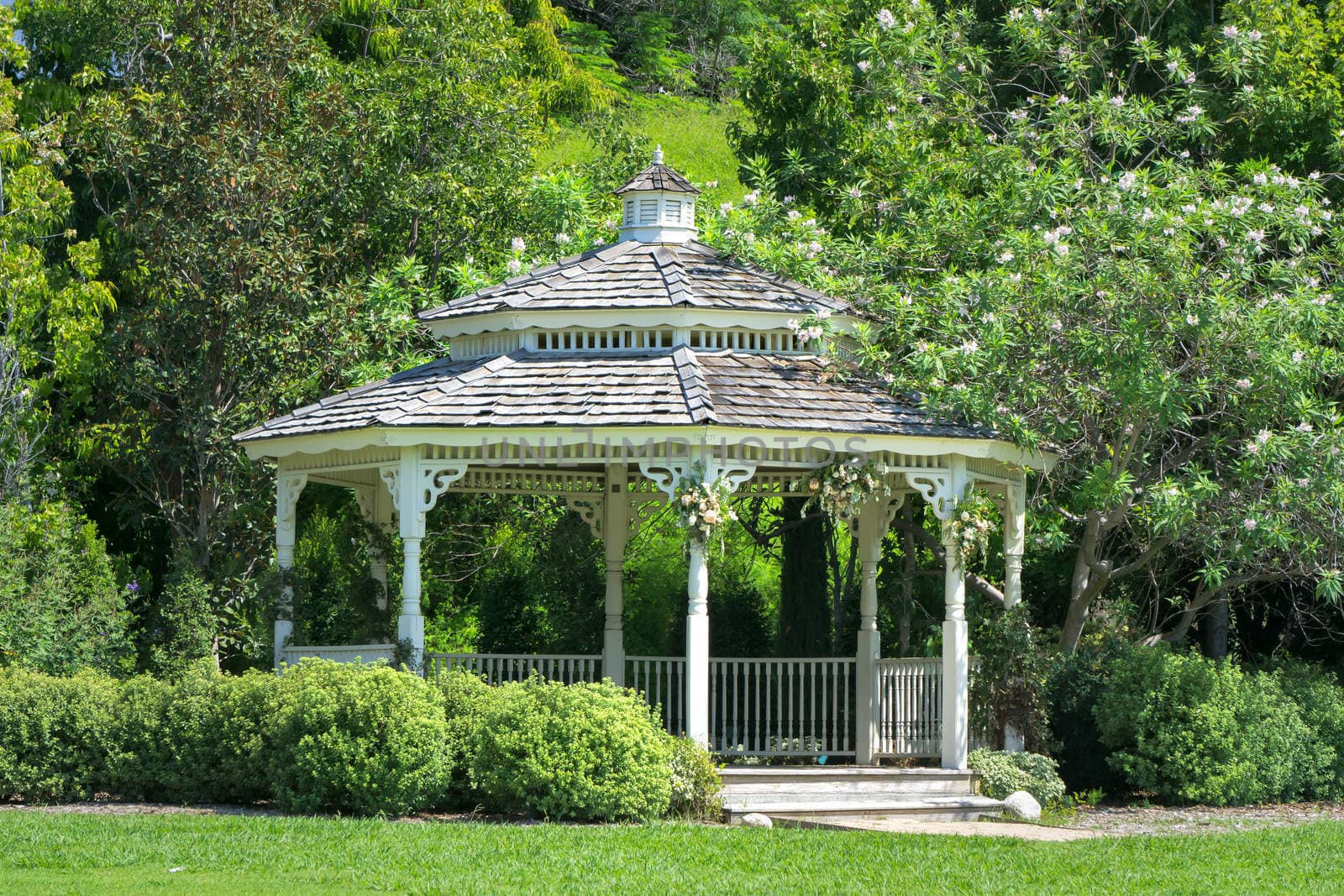 White ornate gazebo structure in green forest with lawn.