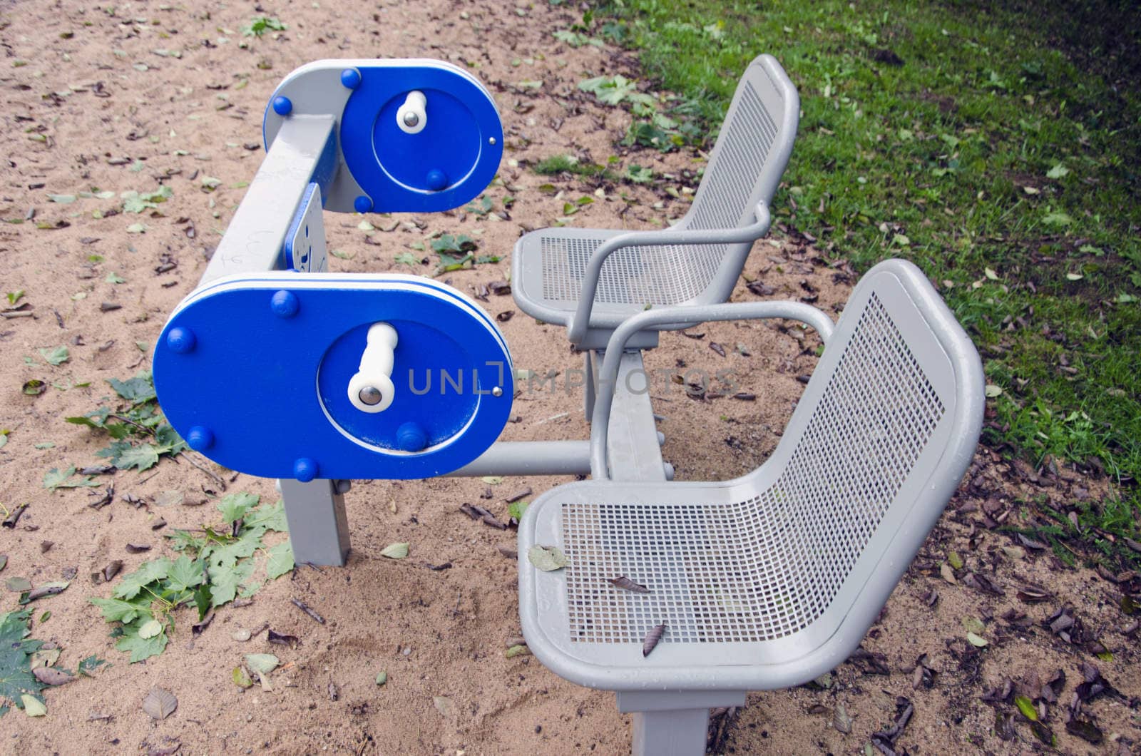 Two metal seats with playground equipment outdoors