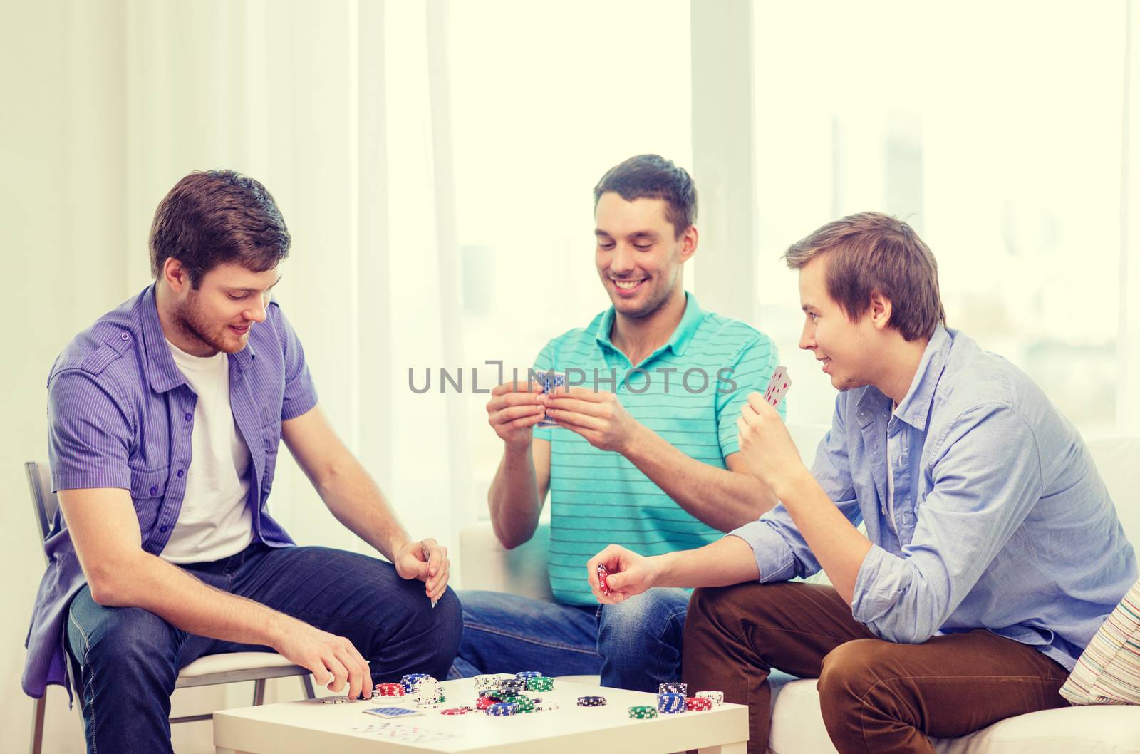 happy three male friends playing poker at home by dolgachov