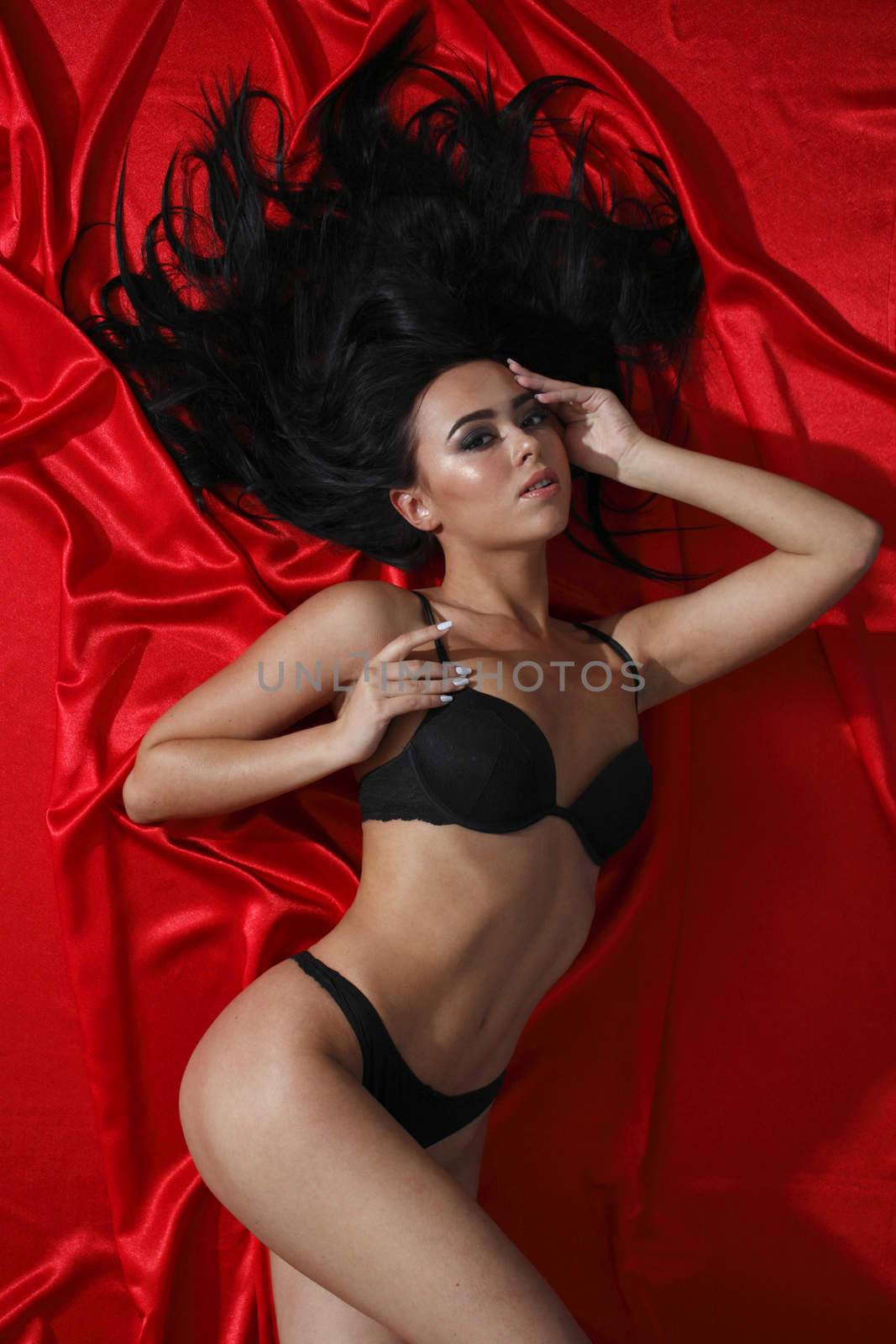Top view of woman in black lingerie laying on red silk