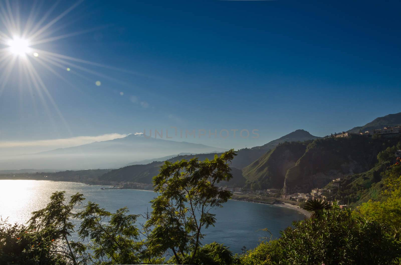 Sicilian seascape from Taormina: mount Etna beyond the blue sea and trees frame on foreground.