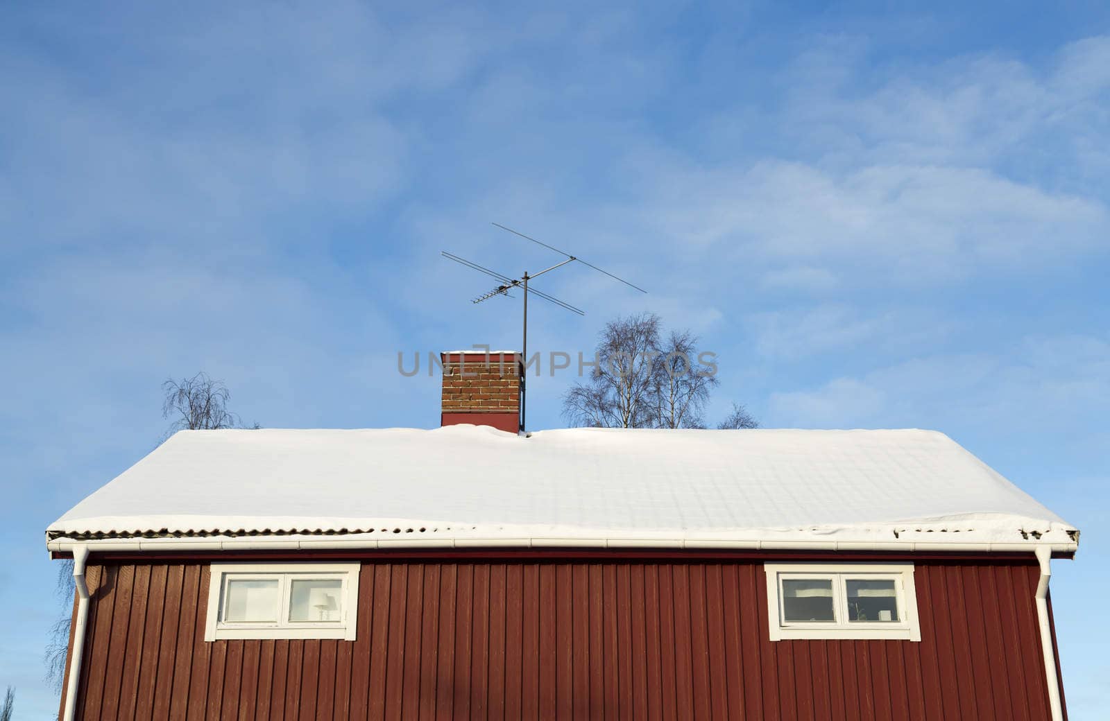 Red House With Snow on the Roof with blue sky and clouds.