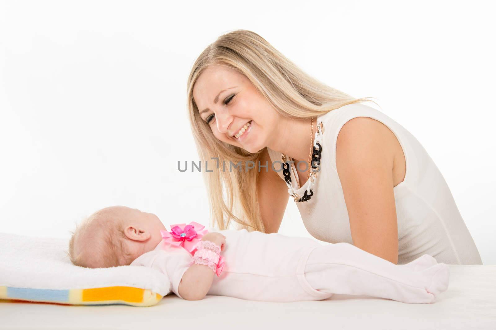 a two-month baby lying on his back on the bed, sitting next to the child and mother looking at her