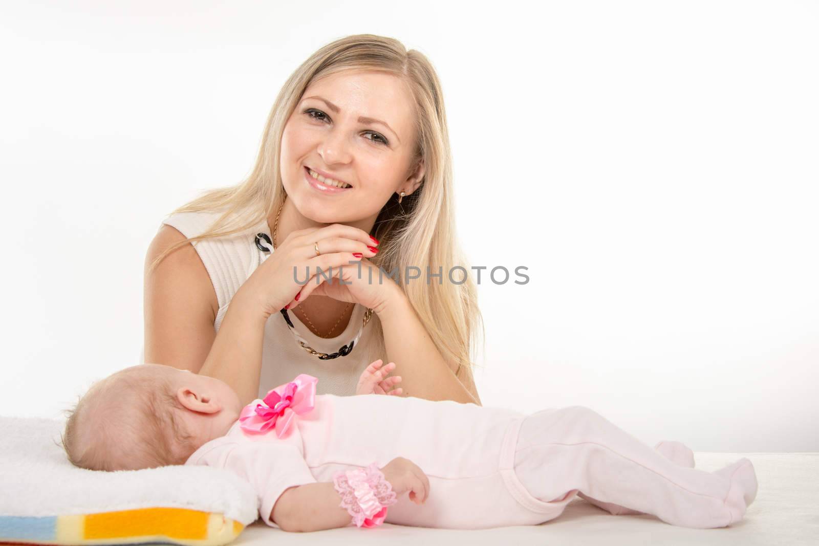 a two-month baby lying on his back on the bed, sitting next to the child and mother looking at her