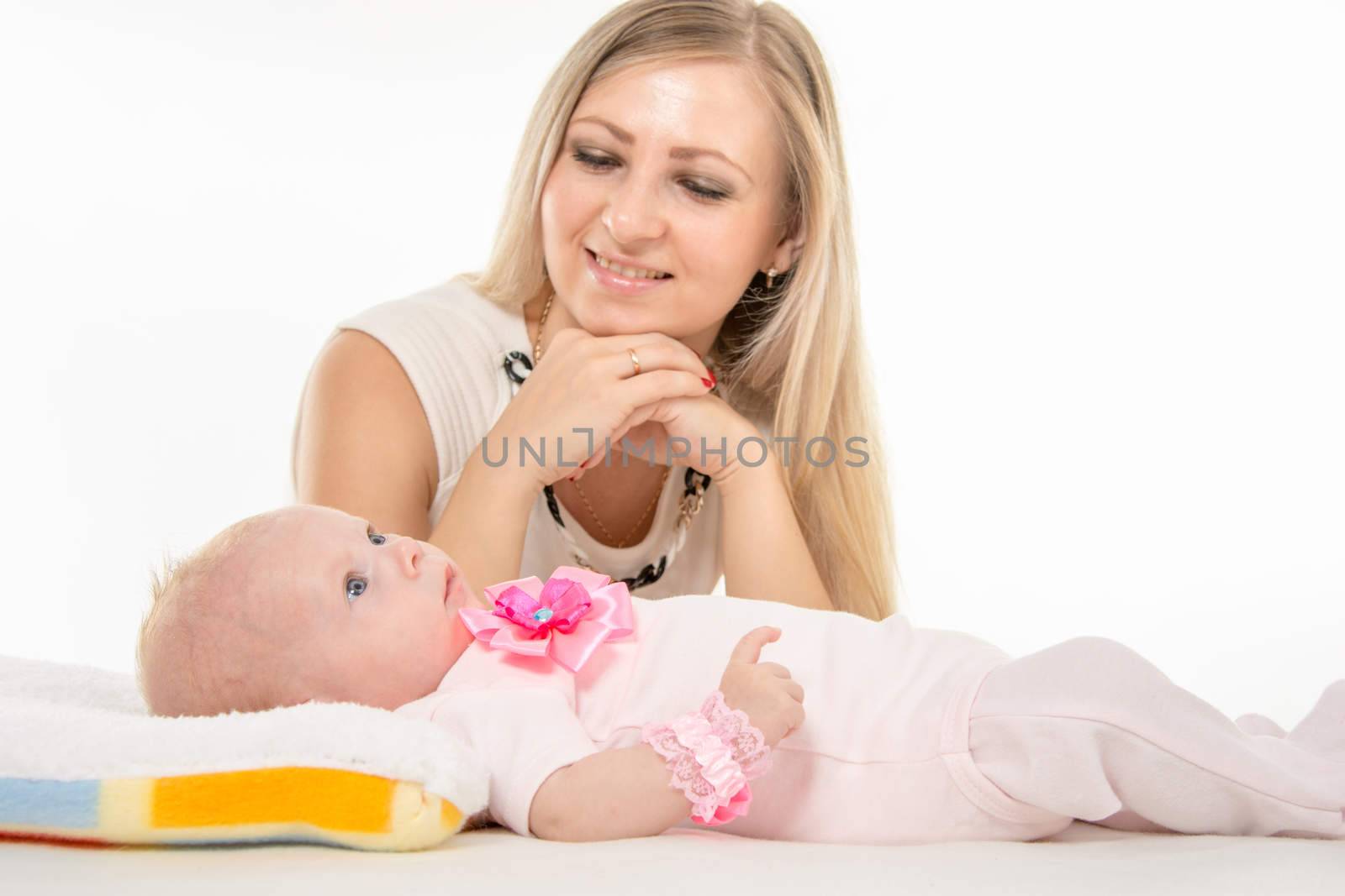 a two-month baby lying on his back on the bed, sitting next to the child and mother looking at her