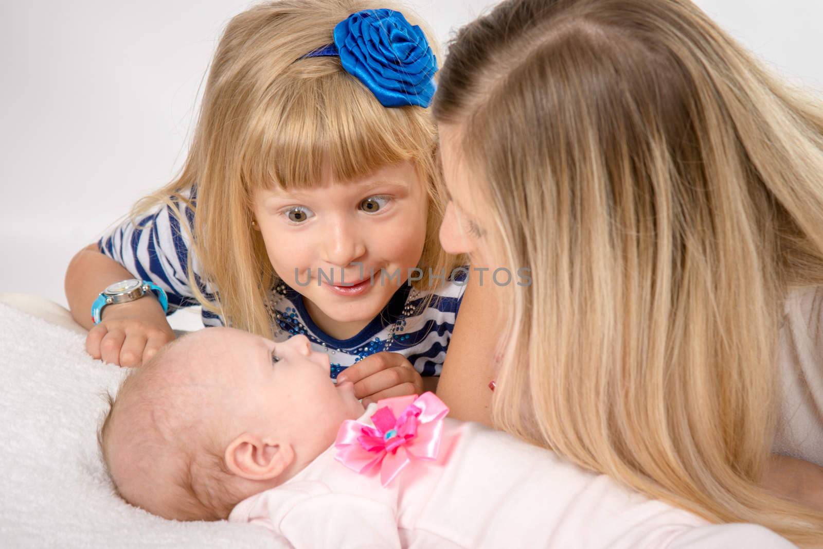 Young mother and daughter sit at the five-year crib, the crib is on a two-month baby on her back