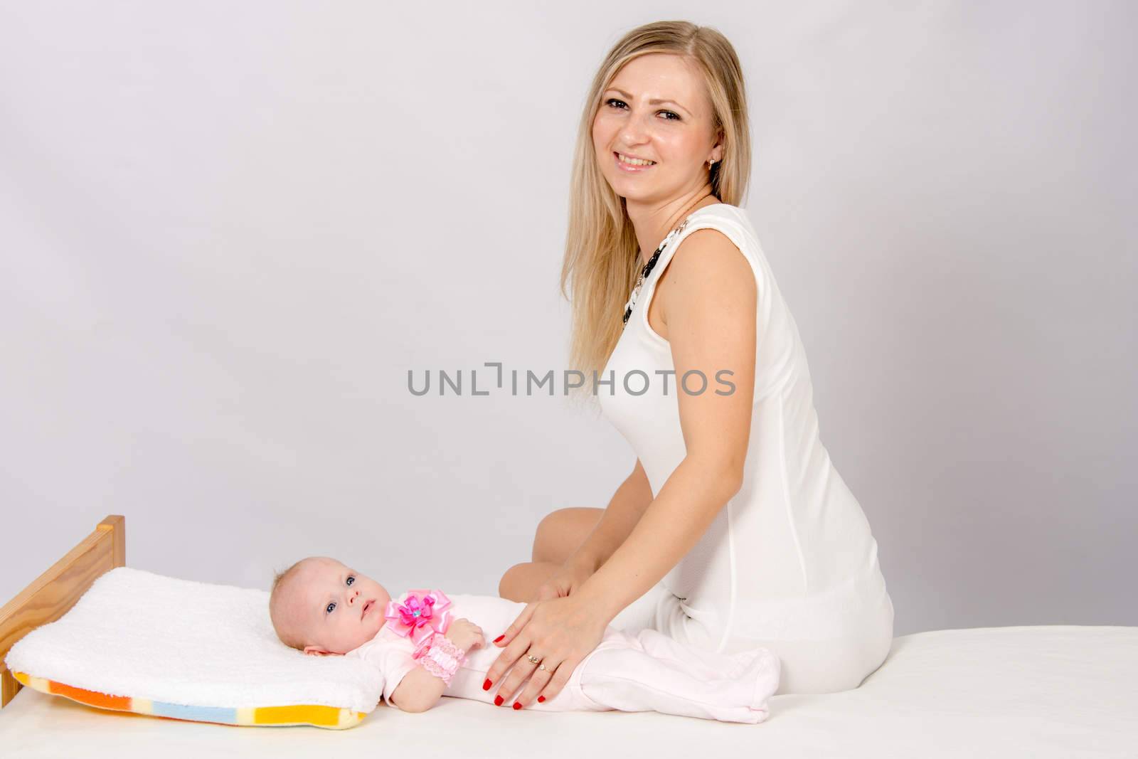 a two-month baby lying on his back on the bed, sitting next to the child and mother looking at her