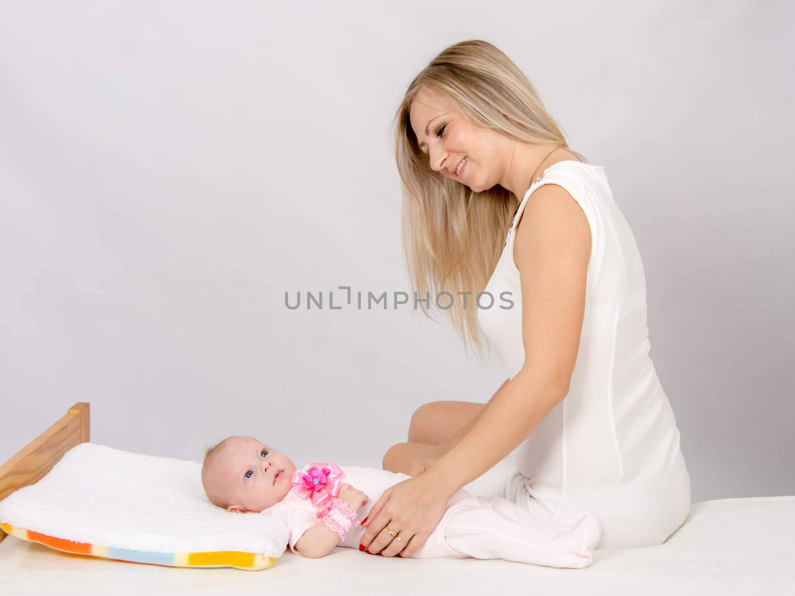 a two-month baby lying on his back on the bed, sitting next to the child and mother looking at her
