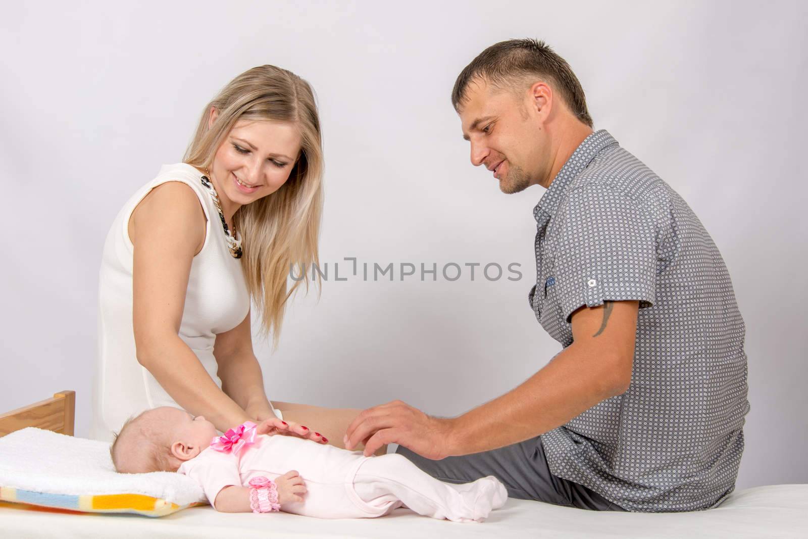 Young parents Mom and Dad sit at the crib, the crib on his back lying on the two-month girl