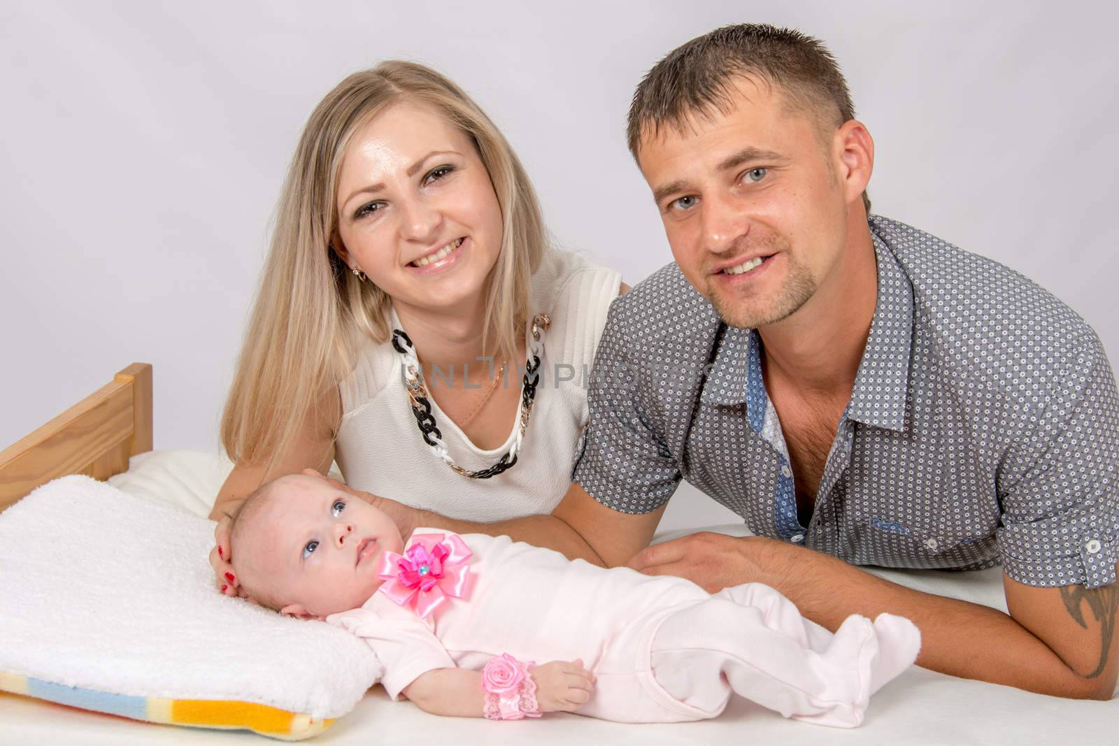 Young parents Mom and Dad sit at the crib, the crib on his back lying on the two-month girl