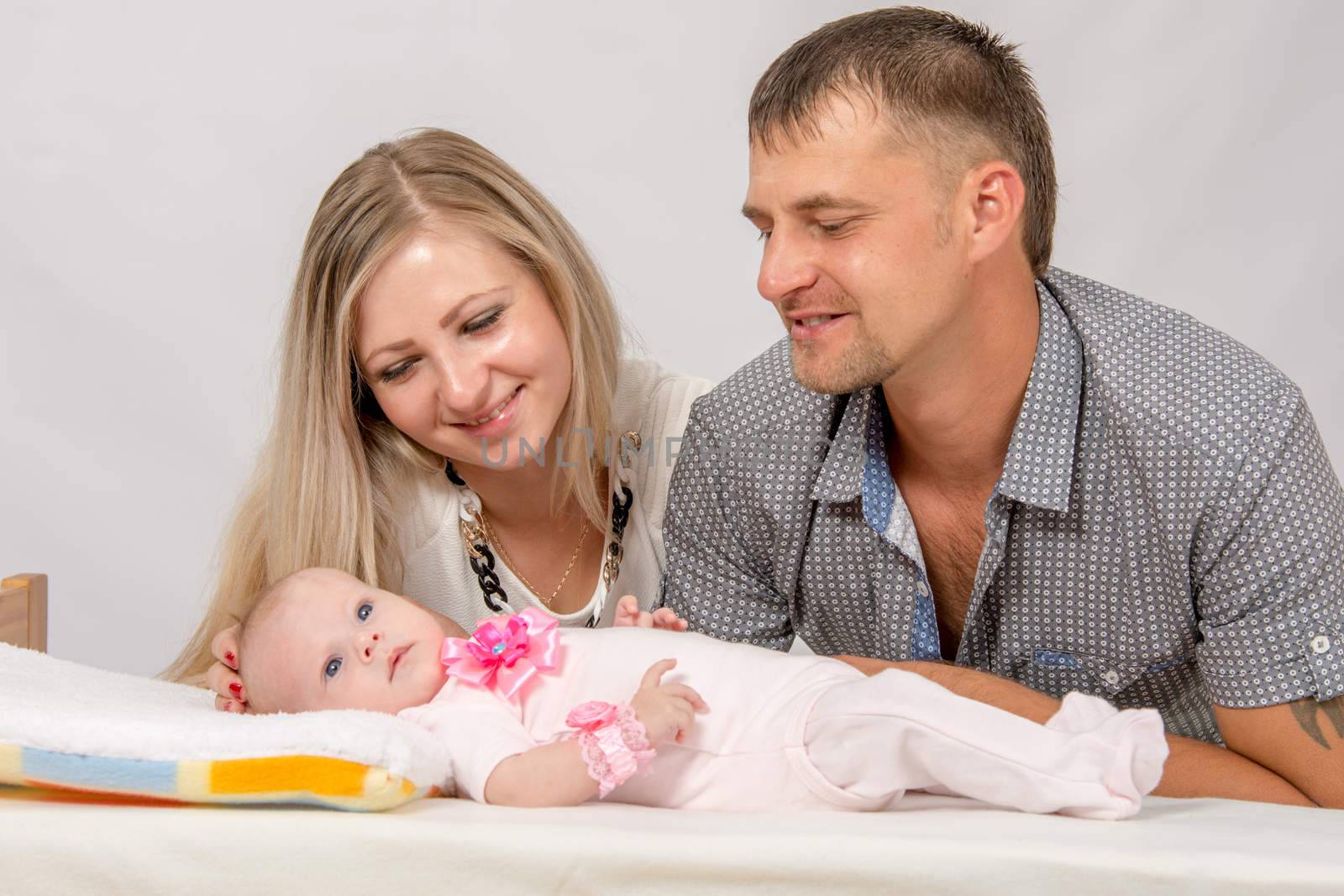 Young parents Mom and Dad sit at the crib, the crib on his back lying on the two-month girl