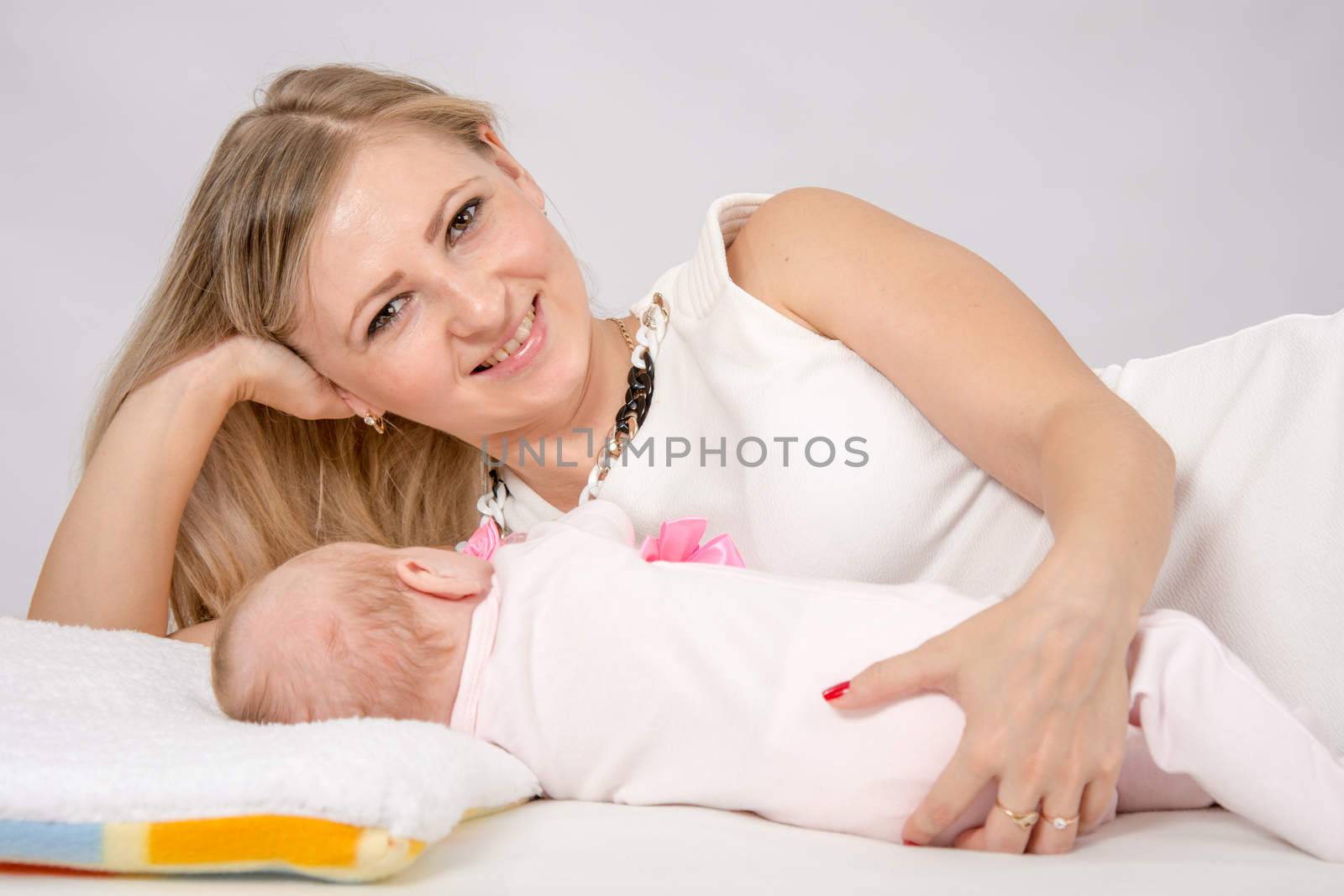 a two-month baby lying on his back on the bed, sitting next to the child and mother looking at her