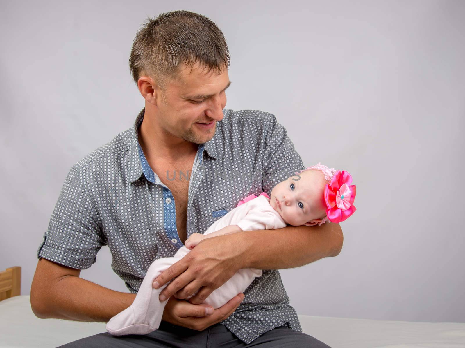 Young dad sitting on a bed and holds her two-month baby daughter